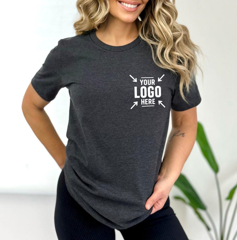 A woman with long, wavy blonde hair is wearing a gray t-shirt with a logo on it.