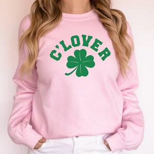 a woman wearing a pink sweater with a clover on it