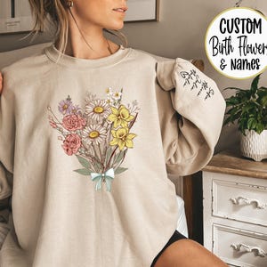 a woman sitting on a bed wearing a sweatshirt with flowers on it