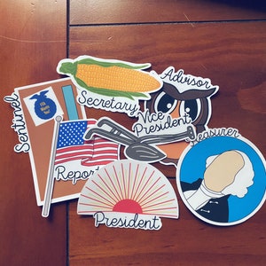 May include: A set of colorful stickers with different designs and text. The stickers include an ear of corn, an owl, a shovel, a sun, a portrait of a man, and a blue circle with the text "Treasurer".
