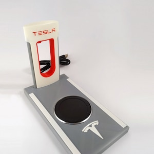 May include: A white and grey charging stand with a red "TESLA" logo and a black wireless charging pad. The stand has a white stripe on each side and a white Tesla logo on the bottom.