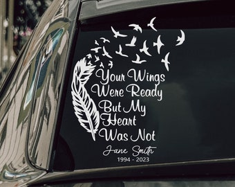 May include: A white vinyl car decal featuring a feather, birds, and the text "Your Wings Were Ready But My Heart Was Not" with a name and dates. The decal is applied to the rear window of a dark gray car.