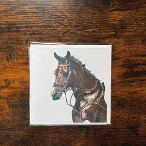May include: A watercolour painting of a brown horse's head and upper body, wearing a bridle and saddle. The horse is set against a white background, with brown speckles. The artwork is on a square card.