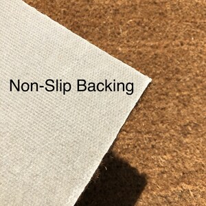 May include: Close-up of a white, textured material labeled "Non-Slip Backing" against a brown, fibrous surface. The white material is angled, revealing its edge and the contrasting texture of the brown background.