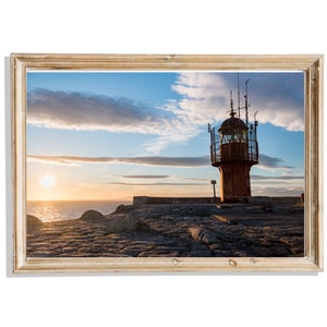 Op de afbeelding: Een rode vuurtoren staat op een rotsachtige kust met een bewolkte blauwe lucht en een heldere oranje zonsondergang op de achtergrond.