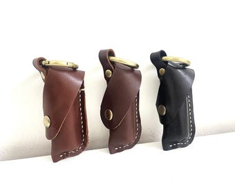 Könnte beinhalten: Drei Leder-Schlüsselanhänger mit Metallringen. Die Schlüsselanhänger sind braun, dunkelbraun und schwarz. Jeder Schlüsselanhänger hat eine Klappe, die mit einem Druckknopf geschlossen wird.