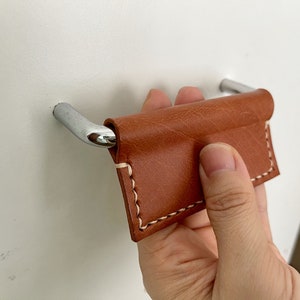 Könnte beinhalten: Ein brauner Leder-Schrankgriff mit weißen Nähten, befestigt an einer silbernen Metallbasis.