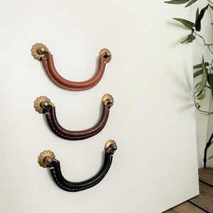 May include: Three leather drawer pulls with decorative brass accents. The pulls are in different colours: brown, dark brown, and black.