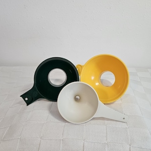 May include: Three plastic funnels in different colors: black, white, and yellow. The funnels are on a white surface.