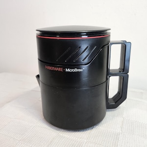 May include: Black plastic coffee maker with a red stripe and the text "FARBERWARE - MicroBrew" on the side. The coffee maker has a handle and a lid.
