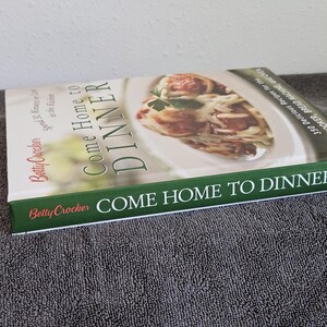 May include: A cookbook titled "Come Home to Dinner" by Betty Crocker. The cover features a photo of a pasta dish with meatballs. The book's spine and cover have green and white text.