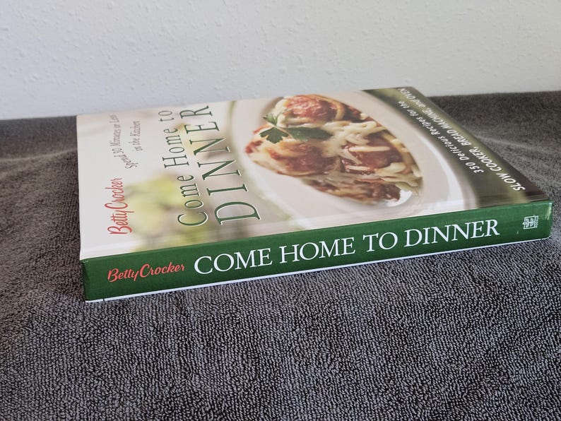 May include: A cookbook titled "Come Home to Dinner" by Betty Crocker. The cover features a photo of a pasta dish with meatballs. The book's spine and cover have green and white text.