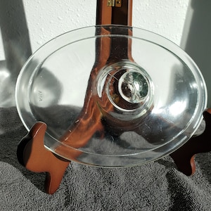 Może przedstawiać: Przezroczysta szklana pokrywka z wypukłym uchwytem w środku. Pokrywka ma owalny kształt i ma nadrukowane słowo "PYREX" na spodzie.