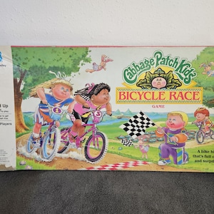 Può includere: Una scatola di gioco da tavolo vintage di Cabbage Patch Kids Bicycle Race. La scatola presenta illustrazioni di Cabbage Patch Kids in bicicletta, con una bandiera a scacchi e il titolo del gioco. La scatola è rettangolare e ha il logo Milton Bradley.