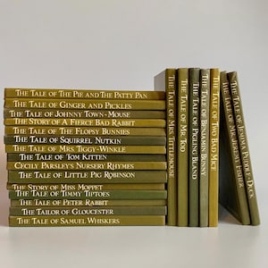 以下が含まれることがあります： オリーブグリーンの表紙のヴィンテージ子供向けの本のコレクション。「ピーターラビットのおはなし」や「ジェマイマ・パドルダックのおはなし」などのタイトルが含まれています。本は積み重ねられ、白い表面に配置されています。