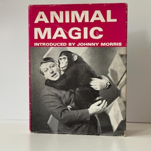 May include: Vintage book cover titled "ANIMAL MAGIC" in white text on a red background. The cover features a black and white image of a man holding a chimpanzee. The text "INTRODUCED BY JOHNNY MORRIS" is below the title.