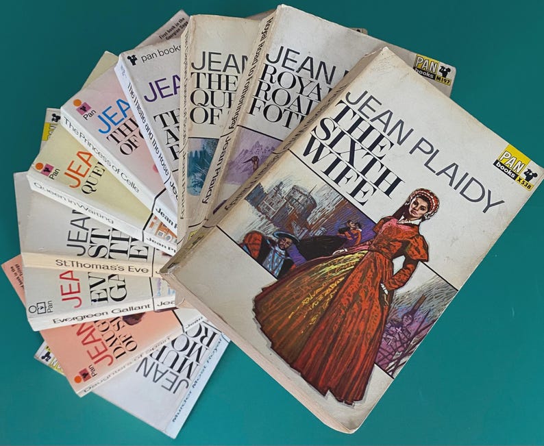 May include: A selection of vintage Jean Plaidy paperback books, arranged in a fan shape. The covers display illustrations and titles including "The Sixth Wife" and "The Road to Fotheringhay". The books are from the Pan Books series.