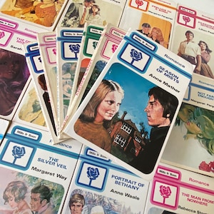 Może przedstawiać: Kolekcja starych romansów Mills & Boon. Okładki przedstawiają ilustracje par, z tytułami takimi jak "Season of Mists" i "The Silver Veil". Książki mają charakterystyczny design z niebiesko-białą obwódką i emblematem róży.