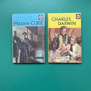 May include: Two vintage Ladybird Books are shown: "Madame Curie" and "Charles Darwin." The "Madame Curie" book has a blue cover with a portrait. The "Charles Darwin" book has a yellow cover with a portrait of the scientist.
