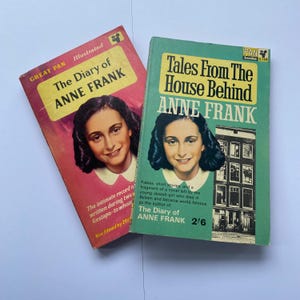 May include: Two vintage paperback books by Anne Frank. One book is titled "The Diary of Anne Frank" with a pink cover and a portrait of Anne Frank. The other book is titled "Tales From The House Behind Anne Frank" with a green cover.