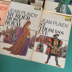 May include: A collection of vintage Jean Plaidy paperback books. The covers showcase illustrations of historical figures and scenes. Titles include "Murder Most Royal" and "St. Thomas's Eve," with the publisher's logo "PAN books" visible.