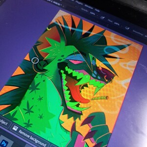 May include: Digital artwork of a green and orange creature with a joint in its mouth. The creature has sharp teeth and is surrounded by a yellow and orange background. The artwork is displayed on a tablet with the Photoshop interface visible.