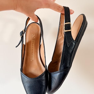 May include: A pair of black leather slingback shoes with a pointed toe and a small heel. The shoes have a buckle closure and the brand name "NATURALIZER" is visible on the insole.