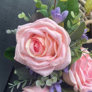 May include: A pink rose with green leaves and purple flowers. The rose is in focus and the background is blurred.