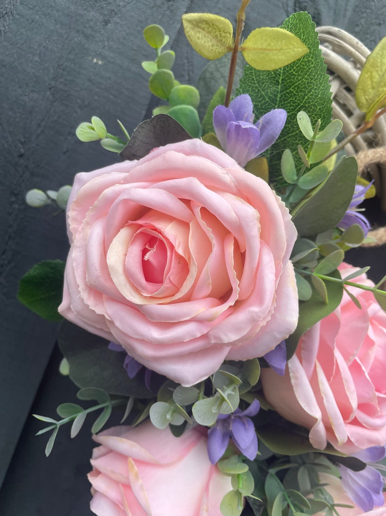 May include: A pink rose with green leaves and purple flowers. The rose is in focus and the background is blurred.