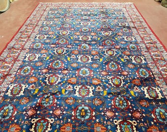 May include: A large, rectangular rug with a deep blue field and an intricate floral pattern in shades of red, orange, and white. The rug has a red border with a repeating design. The overall aesthetic is traditional and ornate.