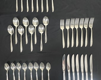 May include: A set of silver flatware, including forks, spoons, and knives. The flatware is arranged in rows on a black surface.
