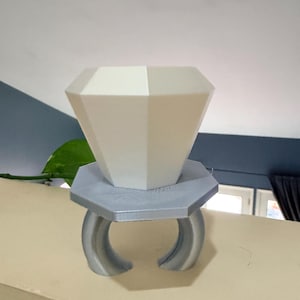 May include: A large, white, geometric diamond-shaped object sits atop a silver ring-shaped base. The base has two curved supports. The object is likely a decorative item or a display piece.