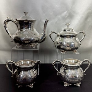 May include: A silver tea set with a teapot, creamer, sugar bowl, and a decorative floral design.