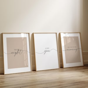 May include: Three vertical framed wall art prints with light wood frames. Each print features a white background with a centered beige rectangle and black text. The text reads: "night night", "love you", and "see you in the morning" in a mix of serif and script fonts.