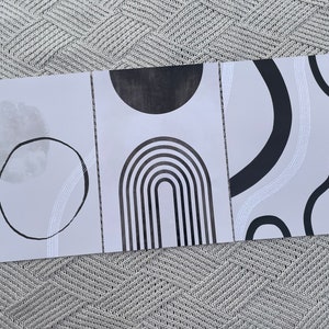 May include: Three minimalist art prints with black and white geometric shapes on a light gray background. The prints feature a circle, an arch, and a series of curved lines.