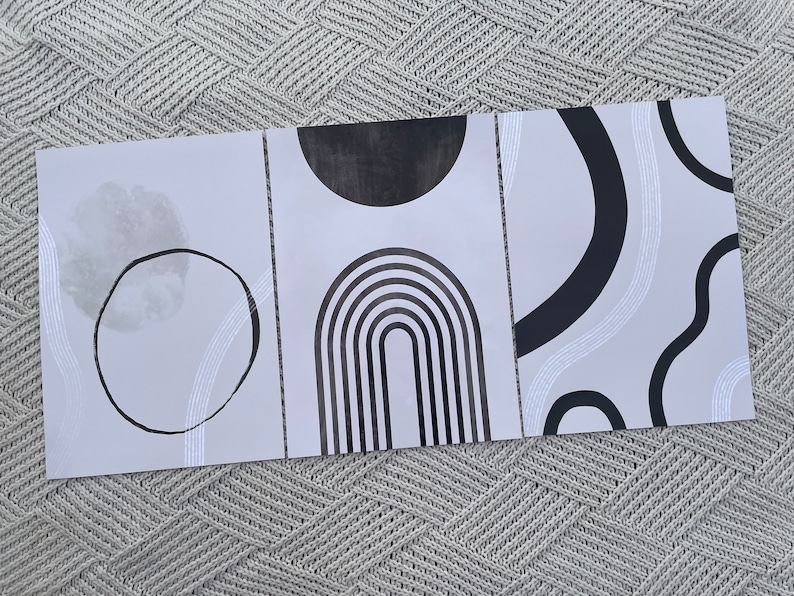 May include: Three minimalist art prints with black and white geometric shapes on a light gray background. The prints feature a circle, an arch, and a series of curved lines.