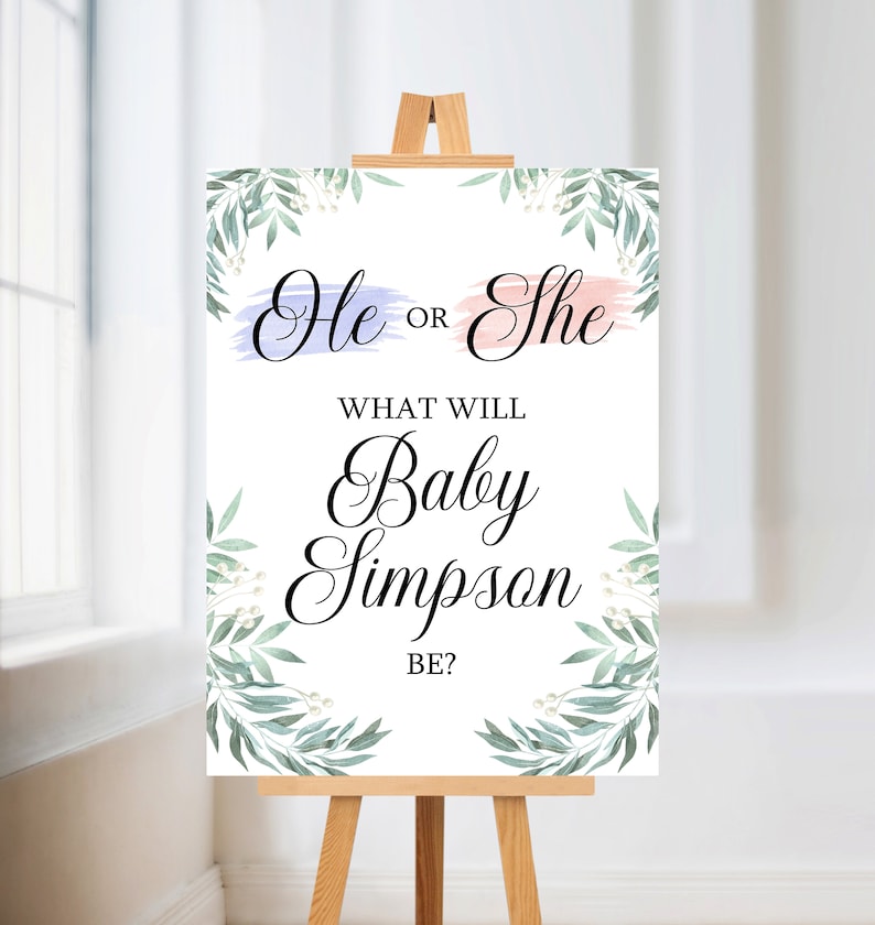 May include: A gender reveal sign with a white background and green leafy branches on the sides. The sign says "He or She" with a blue and pink watercolor stroke behind the words. The sign also says "What will Baby Simpson be?"
