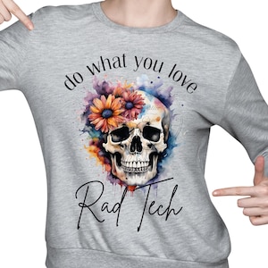 以下が含まれることがあります： 水彩の頭蓋骨と花のデザインが施されたグレーのスウェットシャツ。前面には「do what you love Rad Tech」の文字がプリントされています。