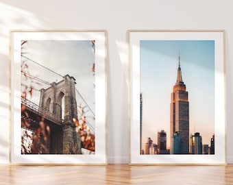 Puede incluir: Dos fotografías enmarcadas de monumentos emblemáticos de la ciudad de Nueva York. La foto de la izquierda muestra el puente de Brooklyn con una vista del horizonte de la ciudad en el fondo. La foto de la derecha muestra el Empire State Building con una vista del horizonte de la ciudad en el fondo.