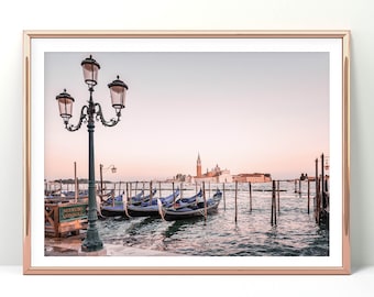 May include: A framed photograph of a scenic view of Venice, Italy. The image features a row of gondolas docked at a pier, with a street lamp in the foreground. The iconic Basilica di San Giorgio Maggiore is visible in the distance, with a soft pink sky in the background.
