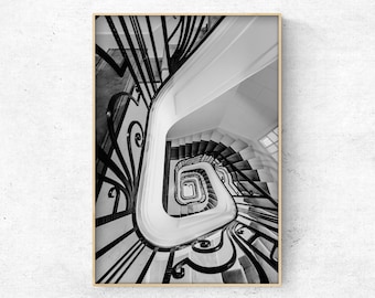 May include: Black and white photograph of a spiral staircase with ornate iron railings. The staircase is seen from above, looking down into the center of the spiral.