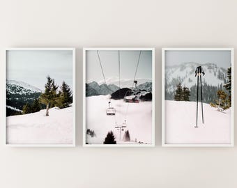 May include: A set of three framed prints featuring snowy mountain scenes. The first print shows a snowy mountain range with a single pine tree in the foreground. The second print shows a ski lift with several gondolas against a backdrop of snow-covered mountains. The third print shows a pair of ski poles resting on a snowy slope.