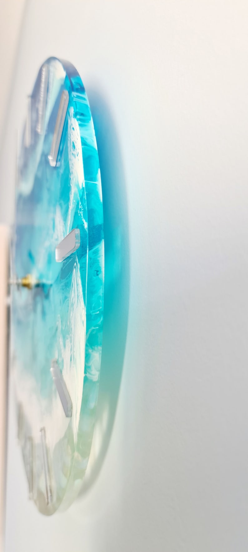 May include: A circular wall clock with a blue and white ocean design. The clock face has a swirling pattern of blue and white resin, with silver markers for the hours. The clock is mounted on a white wall.