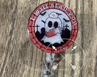 Peut inclure: Un porte-badge rétractable sur le thème d'Halloween rouge et blanc avec un fantôme portant un bonnet d'infirmière et tenant une seringue. Le porte-badge porte le texte "I will stab you" sur le bord. Le porte-badge est attaché à une chaîne argentée avec trois perles : rouge, blanche et noire.