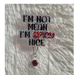 May include: A silver glitter badge holder with the text "I'm not mean I'm spicy nice" in black and red lettering. The badge holder has a red rhinestone on a clear retractable badge reel.