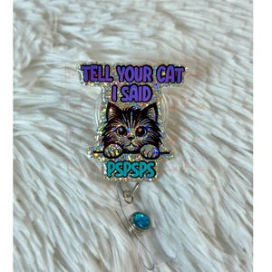 May include: A sparkly purple and silver glitter badge reel with a black cat illustration and the text "Tell your cat I said PSPSPS". The reel has a turquoise blue gem on the retractable cord.