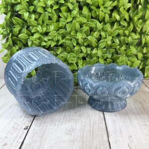 May include: Two blue resin decorative pieces. One is a small, open-topped cylinder with a textured pattern. The other is a small bowl with a pedestal base and a scalloped rim. Both pieces have a marbled appearance.