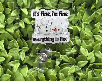 May include: A badge reel featuring a rectangular acrylic topper with a white background and a graphic of two snowmen. The text reads "it's fine, i'm fine" at the top and "everything is fine" at the bottom in black lettering.