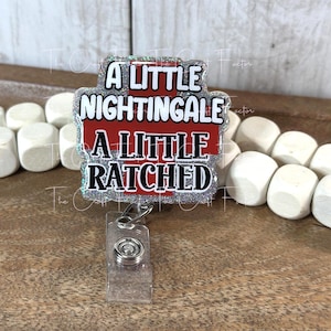 May include: A badge reel with the text "A LITTLE NIGHTINGALE A LITTLE RATCHED" in black and white lettering on a red background, surrounded by a silver glitter border. The reel has a clear plastic clip and a metal clasp.