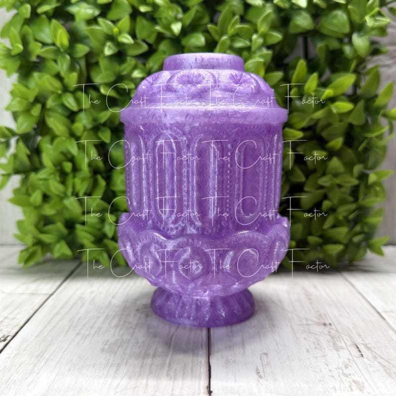 May include: A decorative, purple resin jar with a detailed, ornate design. The jar has a lid and a pedestal base. The Craft Factor is printed on the jar. The background features green foliage and a white wooden surface.